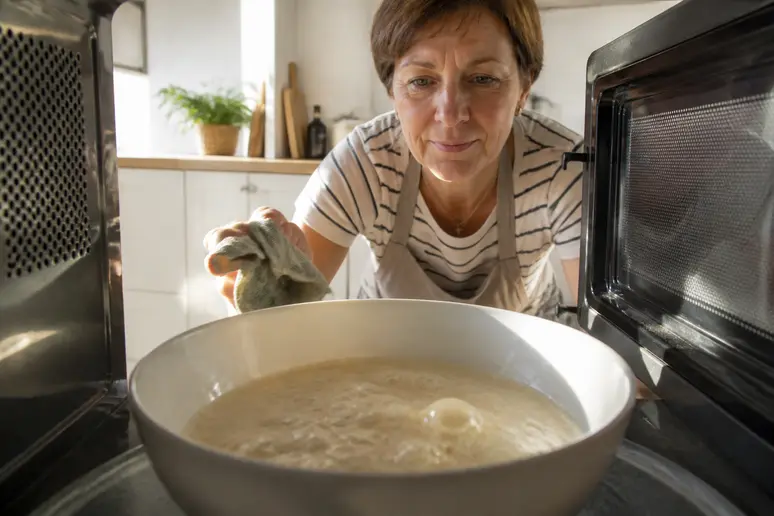 Une femme française au tablier nettoie son micro-ondes avec du bicarbonate et de l'eau bouillante.