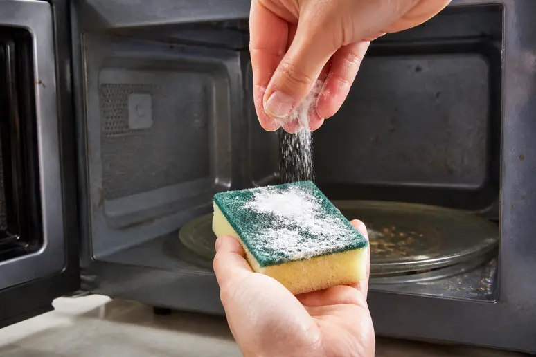 Une éponge humide saupoudrée de bicarbonate de soude est prête à nettoyer l'intérieur d'un micro-ondes.