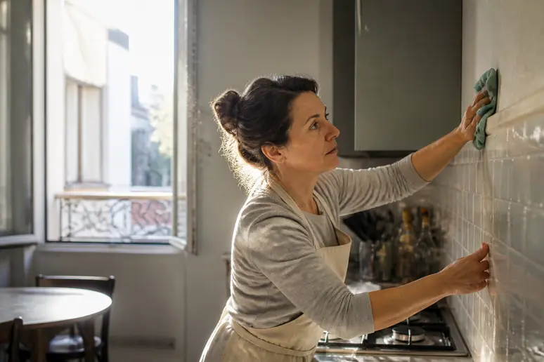 Une femme d'une quarantaine d'années nettoie méticuleusement un mur de cuisine, assurant une préparation parfaite avant la pose.