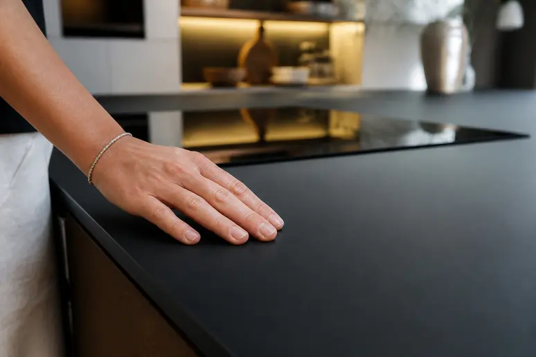 Gros plan sur un plan de travail de cuisine Fenix stratifié noir mat, texture douce et lisse, touché par une main.