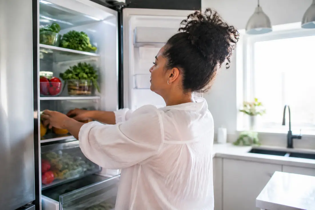 Une personne organise soigneusement des aliments frais dans son réfrigérateur pour savoir comment ranger son frigo efficacement au quotidien.
