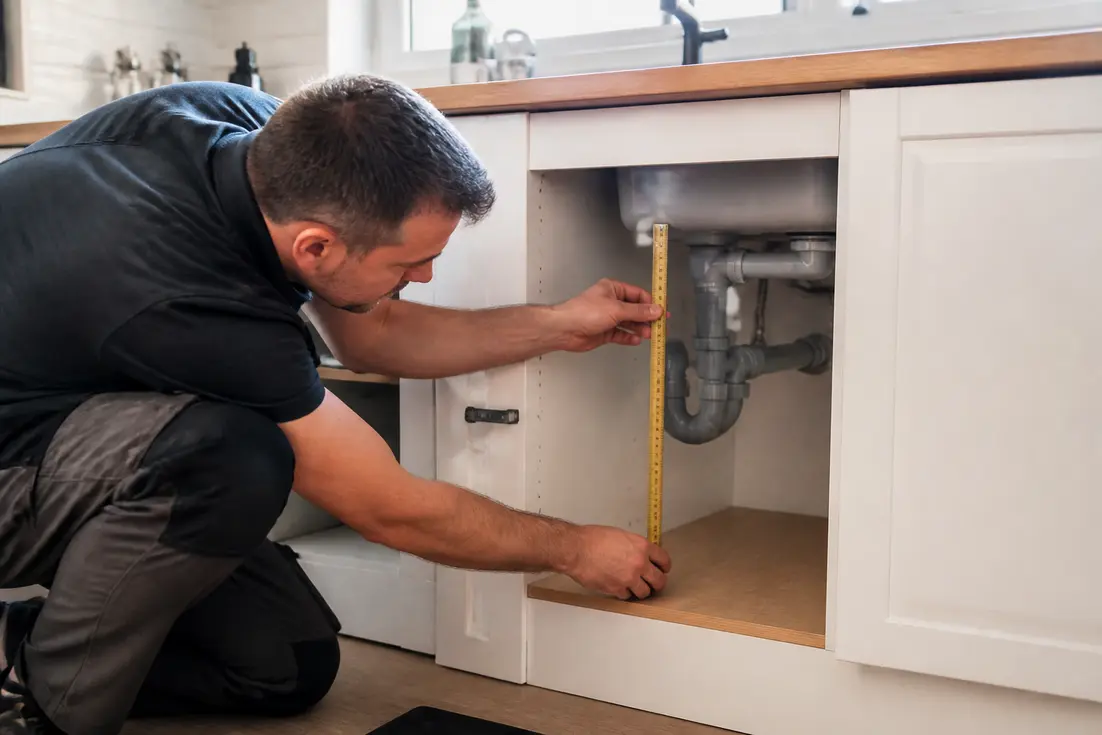 Un plombier ajuste l'installation d'un meuble sous évier dimensions rangement dans une cuisine moderne