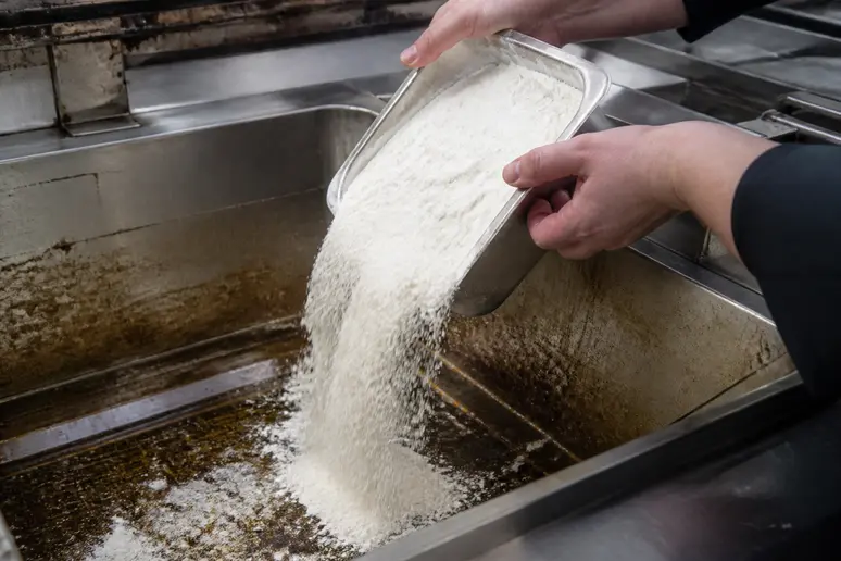 Mains saupoudrant de la farine dans la cuve d'une friteuse pour absorber l'huile usagée