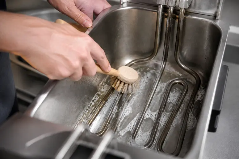 Nettoyage minutieux de la résistance électrique d'une friteuse avec une brosse adaptée